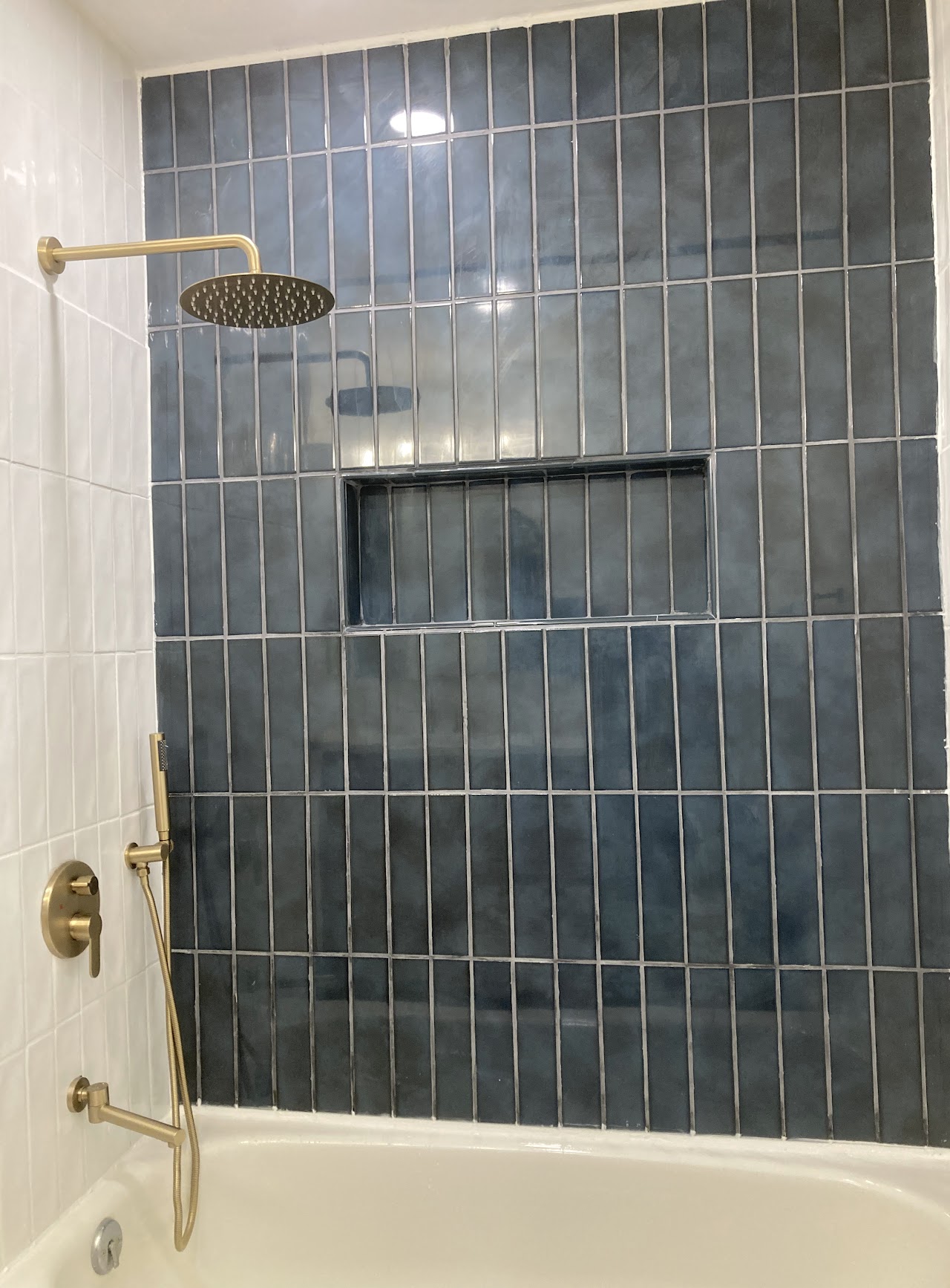 A bath finished in vertical navy tile with a niche and brass fixtures