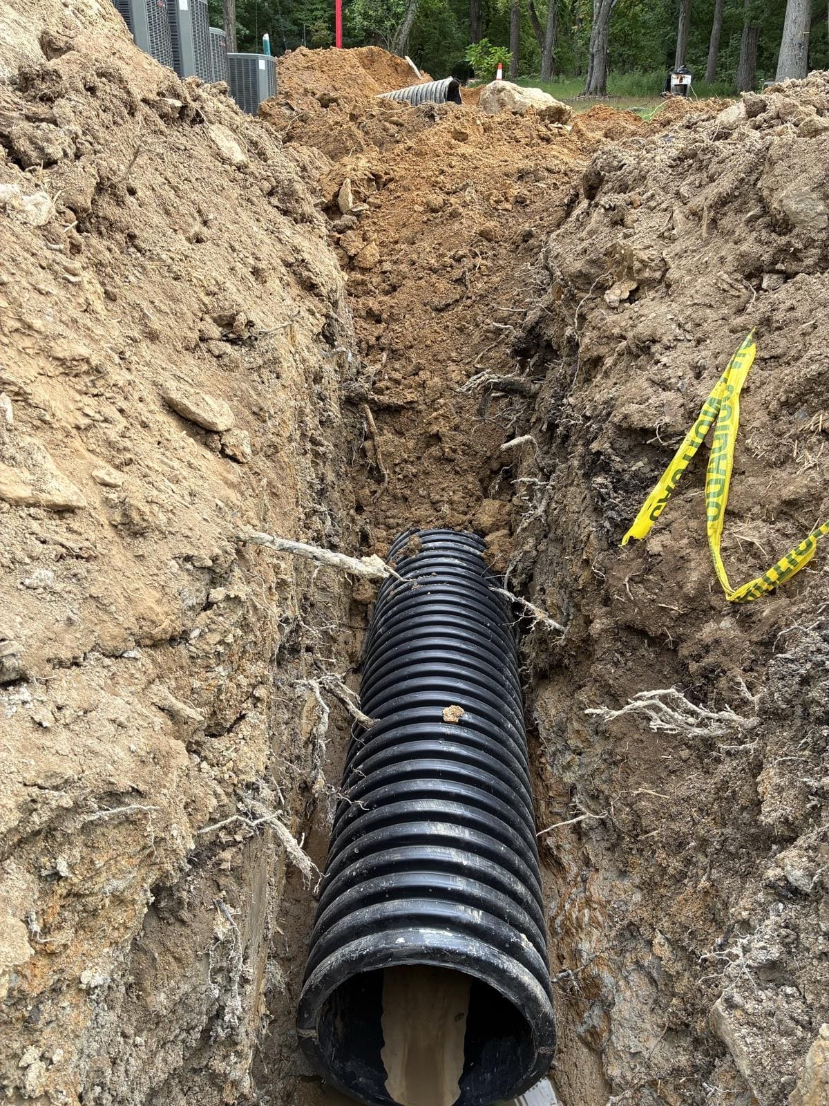 A perforated drain pipe bedded in a stone-lined trench beside a house