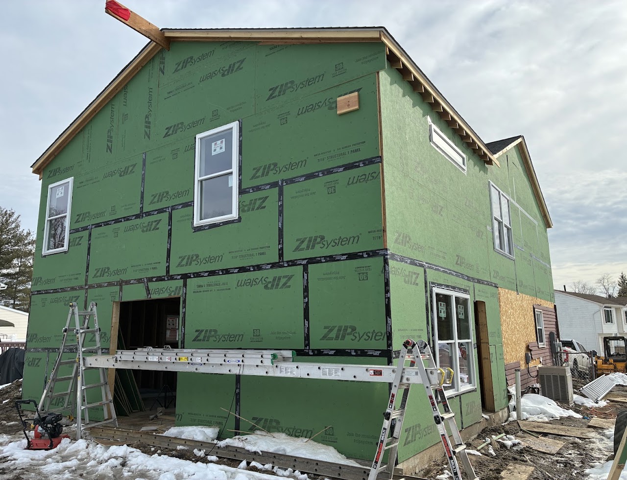 A green-sheathed addition with ladders and staging set along the wall in winter