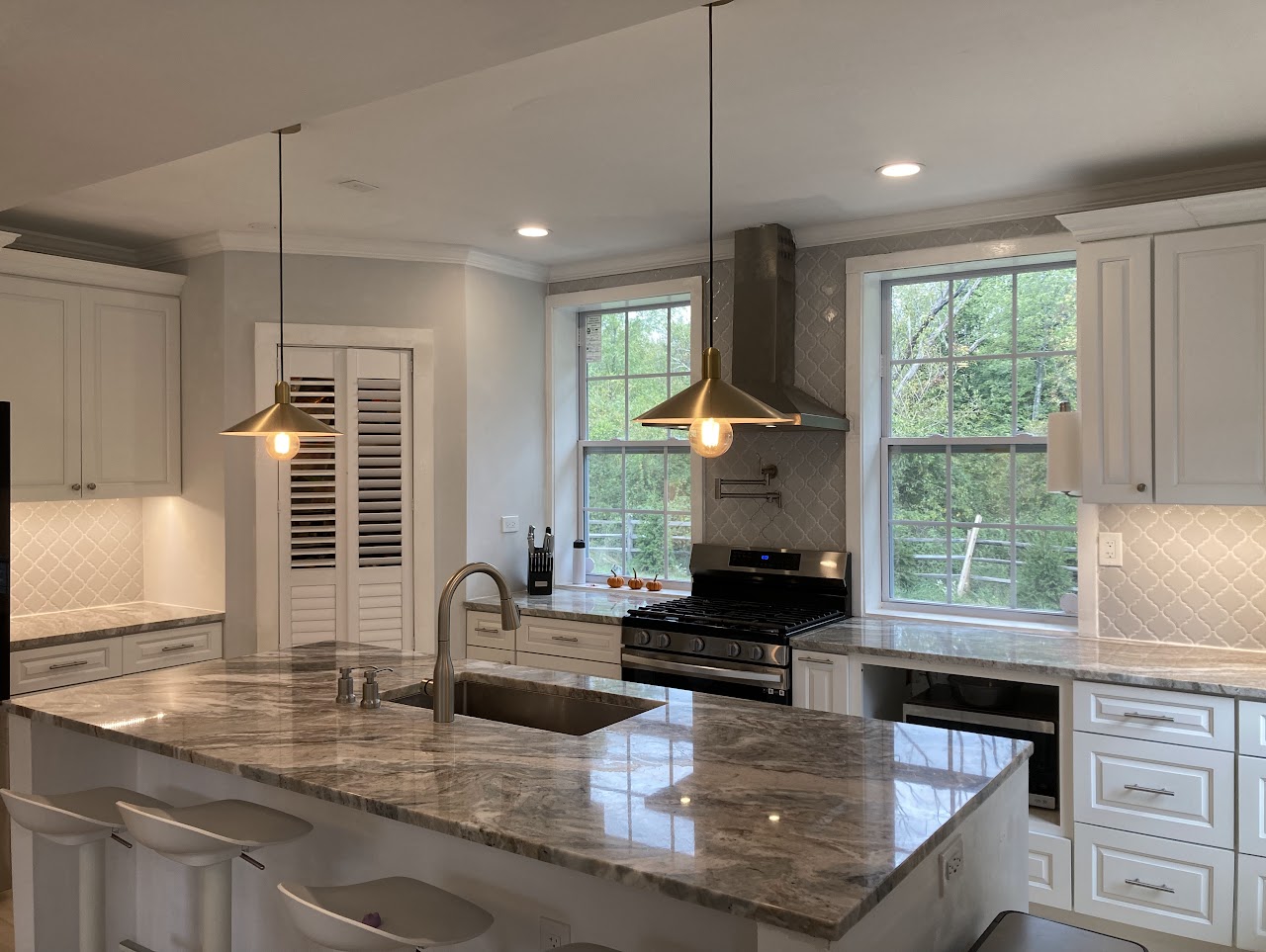 Kitchen with pale cabinetry, stone counters and brass pendants over the island