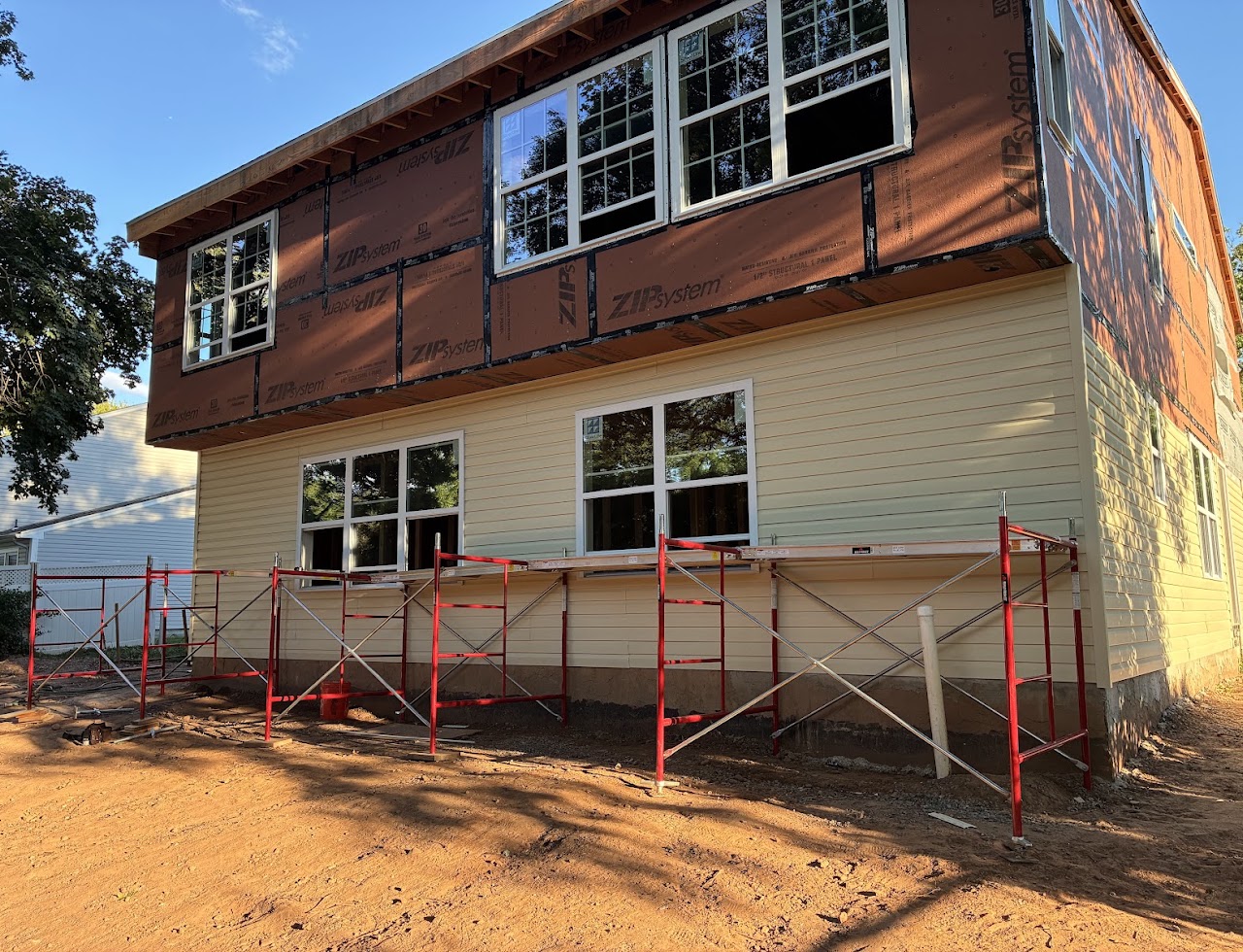 An addition in brown structural sheathing with red scaffolding along the rear wall