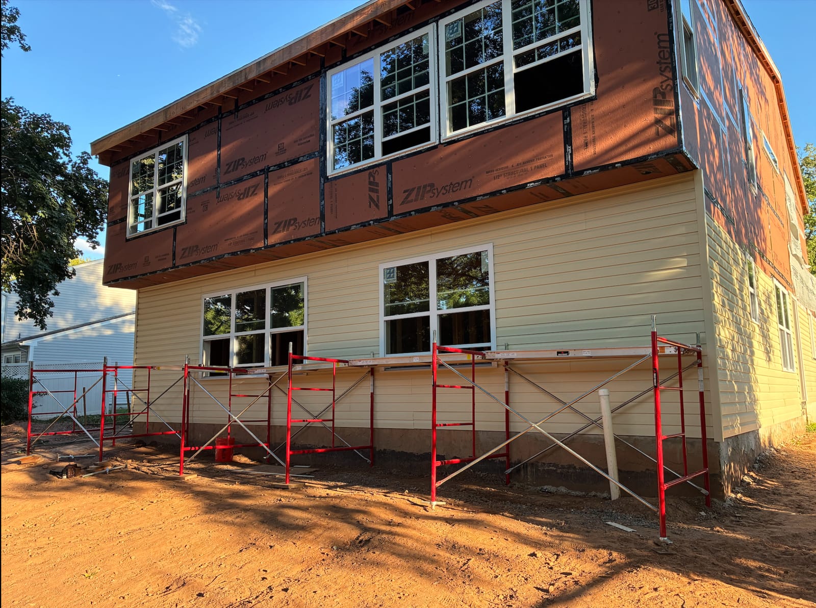 A framed addition in brown structural sheathing standing on red scaffolding